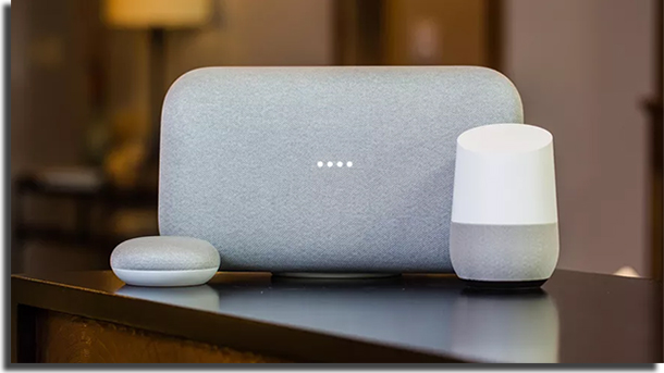 amazon echo, google home and gray soundbar on top of a wooden desk, with a blurred home background